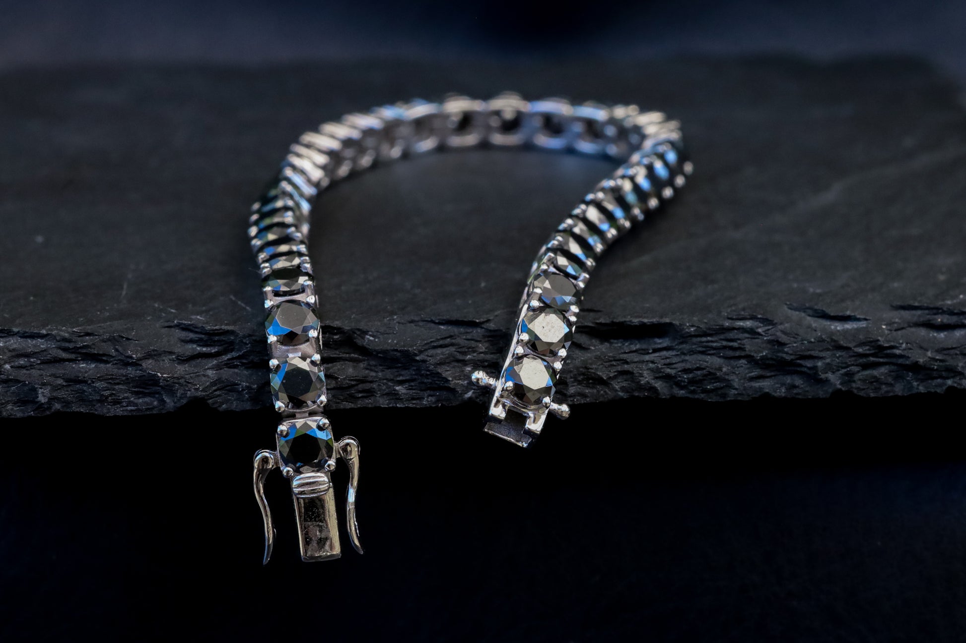 Silver bracelet with black moissanite gem stones on a dark stone surface